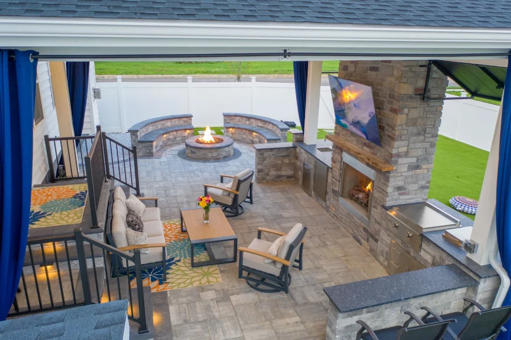 A backyard patio featuring a fire pit, seating, fireplace, TV, and cooking station under cover.